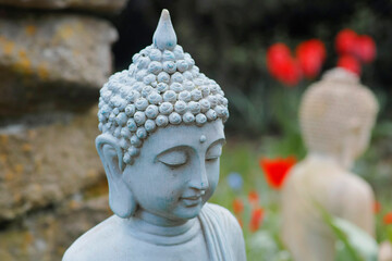 Portrait of a garden buddha with red tulips and another buddha blurred in the background