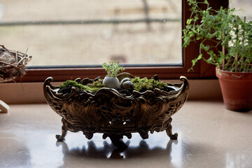 A massive bronze vase on legs with moss, greenery sprouted in an egg. A new life - 778403987