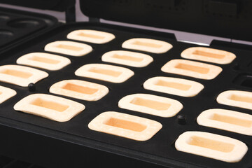 A tray of baked goods with a black background. The baked goods are in the shape of squares and are arranged in a neat row