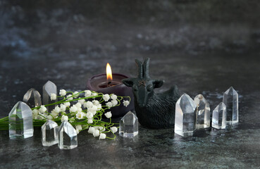 amulet in goat form, candle, crystals and flowers on table, dark background. witch black goat -...