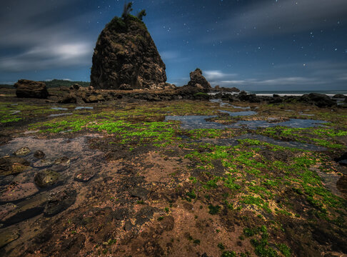 Rock beach night photography with starry blue sky background and cloud motion blur