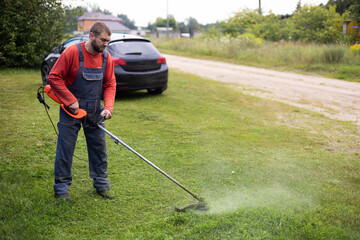 A man uses an eco-friendly electric trimmer to cut the grass in his front lawn. A man mows the...