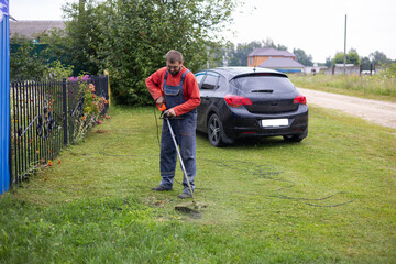 A man mows the grass in front of his house with a lawnmower. A man mows the grass on his lawn with an electric lawn mower. Lawn care and grass cutting with a lawn mower.