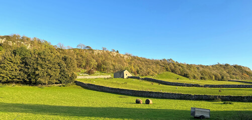 A serene landscape bathed in the warm glow of sunlight, with a solitary building nestled among green fields and dry stone walls in Stainforth, Settle, UK.