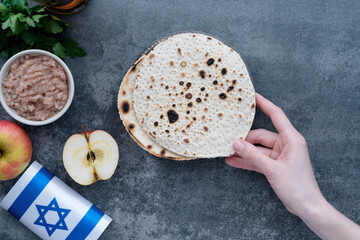 Human hands holding handmade round Matzah in a plate on a concrete background. Saved Jewish Pesach...