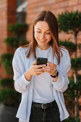 Vertical shot of an ecstatic smiling woman using her smart phone near a brick wall.