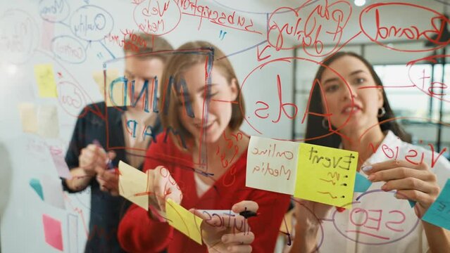 Creative business team brainstorming and sharing marketing idea about start up project by writing down on colorful sticky note at glass board modern meeting room. Working together. Immaculate.