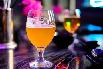 Two glasses of beer stand on a table opposite bright pink flowers at background