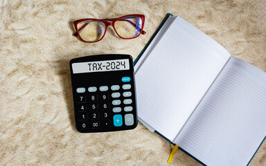 The word Tax 2024 on a calculator. Business and taxation concept. Calculator, book, glasses on the...