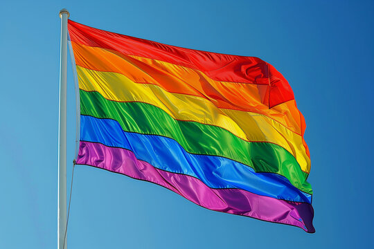 A rainbow flag is flying in the sky. The flag is colorful and vibrant, representing the LGBTQ+ community. The blue sky in the background adds to the cheerful and uplifting mood of the image