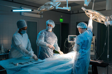 Wide shot of doctor in surgical uniforms and masks adjusting light before operation in dark operating theatre. Surgery, hospital, medical and healthcare services. Concept of surgery and emergency. - Powered by Adobe