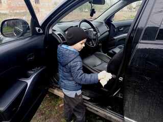 A six-year-old boy cleans the interior of a black car. Child labor. A child wipes dust in the car interior. The father entrusted the cleaning of the car to his son.