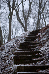 Weathered concrete steps leading up a hill, symbolizing human challenges, hardships, and hard work. Gloomy winter day with snow reinforces the association.
