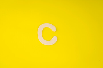 Letter C in wood on yellow background