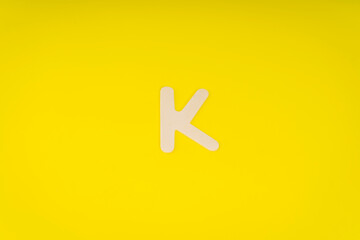 Letter K in wood on yellow background