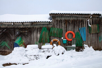 Old wooden sheds by the lake. Everything is covered in snow, and the colorful parts of wooden boats scattered around break the winter monotony... Trakai, Lithuania.