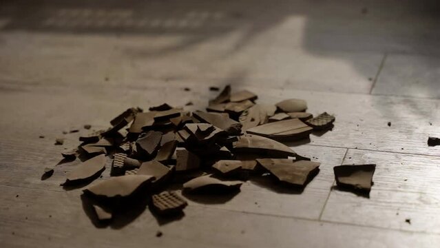 Close-up of ceramic fragments on wood floor, aftermath of pottery breaking