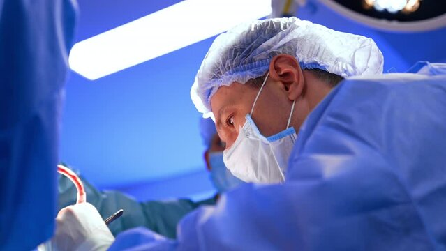 Concentrated look of a male Caucasian surgeon in mask and cap holding the instruments. Low angle view on the doctor carrying out the neurosurgery.