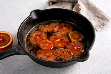 Traditional orange tasty sauce for French crepe Suzette in a cast iron pan on light table.