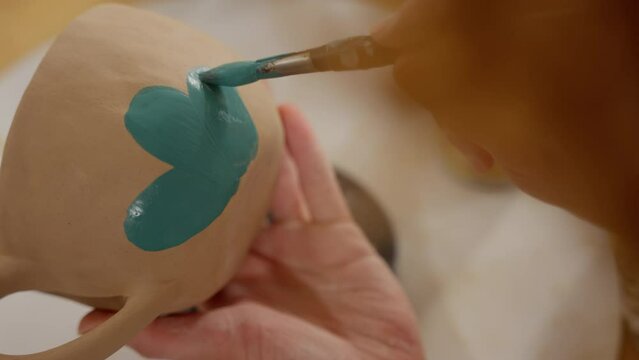 Close-up of a hand painting a flower design on a pottery piece with vibrant glaze