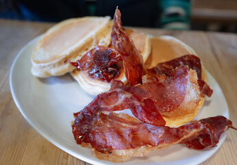 Crispy, curly ham and pancakes on a white oval plate on a wooden table.  - 778472156