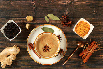 Indian masala chai tea with milk, ginger, anise and cinnamon on an old wooden table. Traditional drink with spices, cafe concept, advertising for restaurant and menu.
