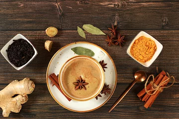 Keuken spatwand met foto Indian masala chai tea with milk, ginger, anise and cinnamon on an old wooden table. Traditional drink with spices, cafe concept, advertising for restaurant and menu. © Светлана Балынь