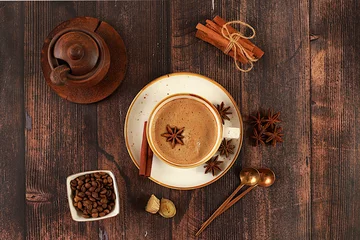Zelfklevend Fotobehang Cup of coffee with milk, ginger, anise and cinnamon on an old wooden table. Traditional Indian drink with spices, cafe concept, advertising for restaurant and menu. © Светлана Балынь