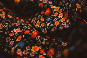 Fototapeta na wymiar Multicolored fabric with a print of many colorful flowers. Warm summer floral pattern. Dark black fabric texture. Female fashion and glamour vintage.