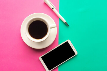 Flat lay photo with coffee cup, mobile phone and pen on geometric green and pink background. Top...