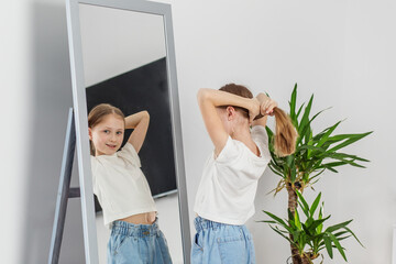 Girl Tying Hair in Front of Mirror. Morning preparation before school.