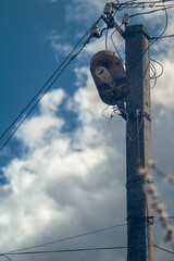 An electric pole with a street lamp on the background of the sky with clouds