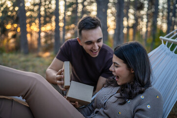 Young couple man and woman give present gift box while sit in nature