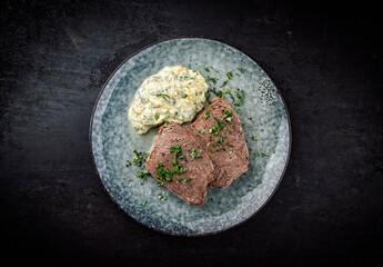 Cooked roast veal with sour cream sauce, eggs and chopped herbs served as top view on a Nordic design plate