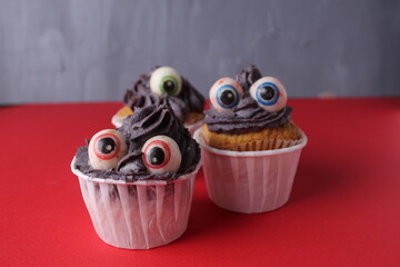 Three cupcakes with eyes on a red background. Funny Cakes For Kids Halloween Party With Space For Copy Space Text