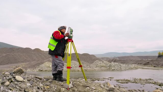 Surveyor is using newest geological equipment to analyze area. Surveyor is operating the geological theodolite equipment with moveable telescope. Surveyor measuring quarry using geological equipment