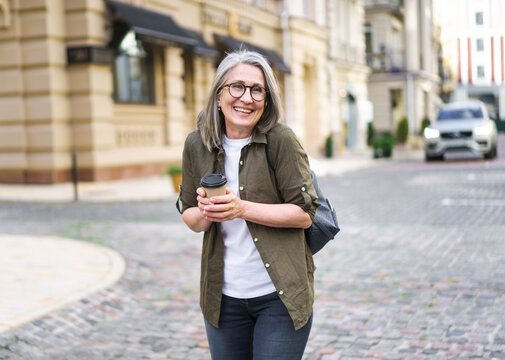 A woman is walking down a street holding a coffee cup. She is smiling and she is in a good mood