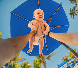 Dad and baby share a tender moment under a beach umbrella, palm trees framing their peaceful bonding