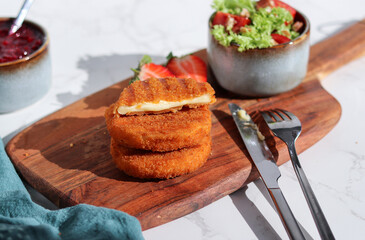 Fresh made and cutted fried camembert cheese with a side of fresh salad on wooden plate, white marble table