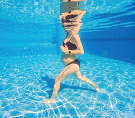 Embracing aquatic fitness, a pregnant woman demonstrates strength and serenity in underwater aerobics, creating a serene and empowering image in the pool - obrazy, fototapety, plakaty