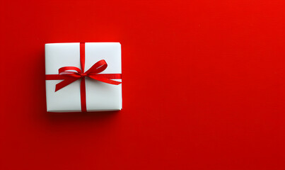 Gift box wrapped in white paper with golden ribbon bow on the red background. Good for Christmas, Valentine's Day, Mother's day or Birthday. Copy space.