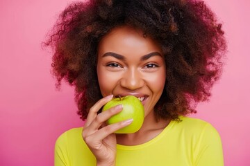 Beautiful smiling woman in bright yellow top biting crisp green apple, isolated on pink background, concept of happiness and healthy eating