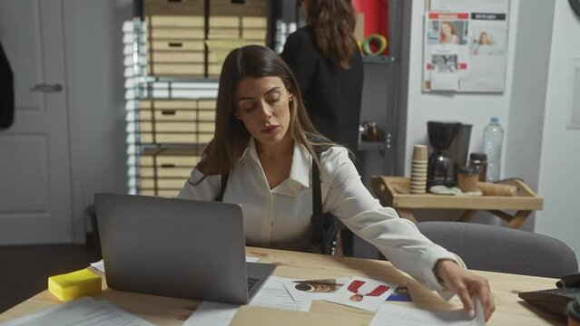 Two women in an office with laptops, documents, and evidence examining passports and ids during an investigation.