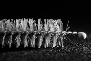 a black and white photo of a tube brush with a feather on a dark background.