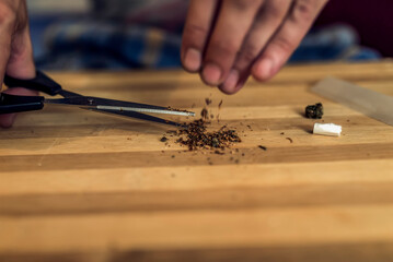 Close up at the Hands of an Adult Caucasian Man Rolling a Marijuana Joint. Preparing and Rolling Marijuana Cannabis Joint. Drugs Narcotic Concept. Close up.