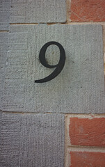 Metal number nine or 9 coated with black paint applied in Latin letters to the building. Brick...
