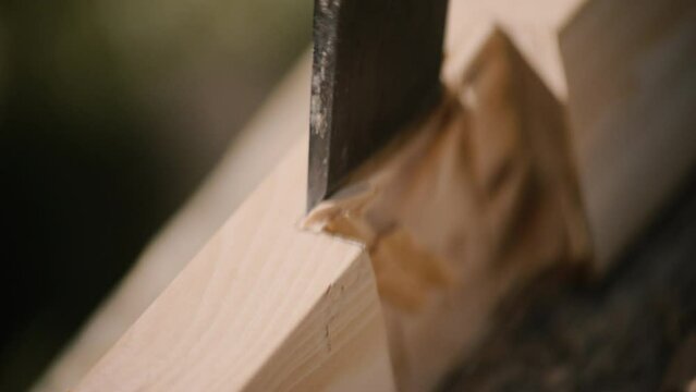 Carpenter using mallet and chisel for wooden cross made by hand in sunlight.