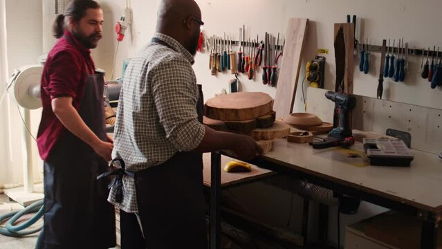 Manufacturer selecting tool from rack to use on wood materials, ensuring it aligns with project requirements. Cabinetmaker doing quality assurance on lumber pieces pile, picking best one for