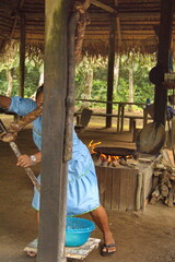Indigenous woman squeezing yuca to make bread in an outdoor kitchen in Puerto Bolivar in the Cuyabeno Wildlife Reserve, outside of Lago Agrio, Ecuador - obrazy, fototapety, plakaty