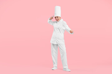 Happy professional confectioner in uniform holding whisk and spatula on pink background